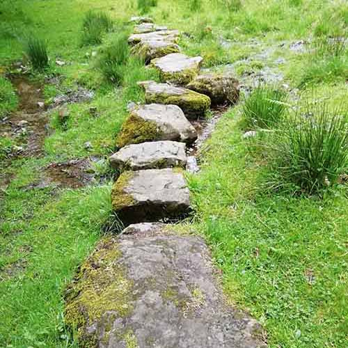 A water stream passing through some rocks on a grassy hill